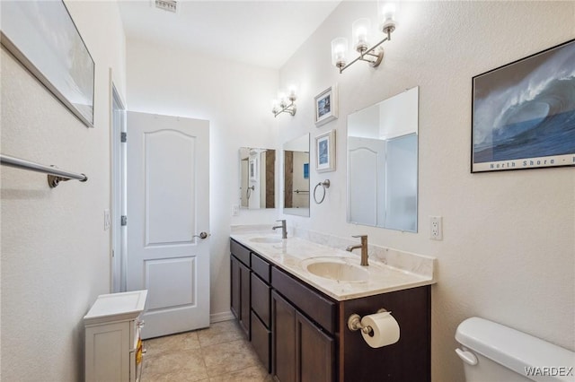 full bath with toilet, double vanity, a sink, and tile patterned floors