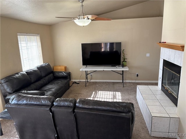 carpeted living area with ceiling fan, a tiled fireplace, and baseboards