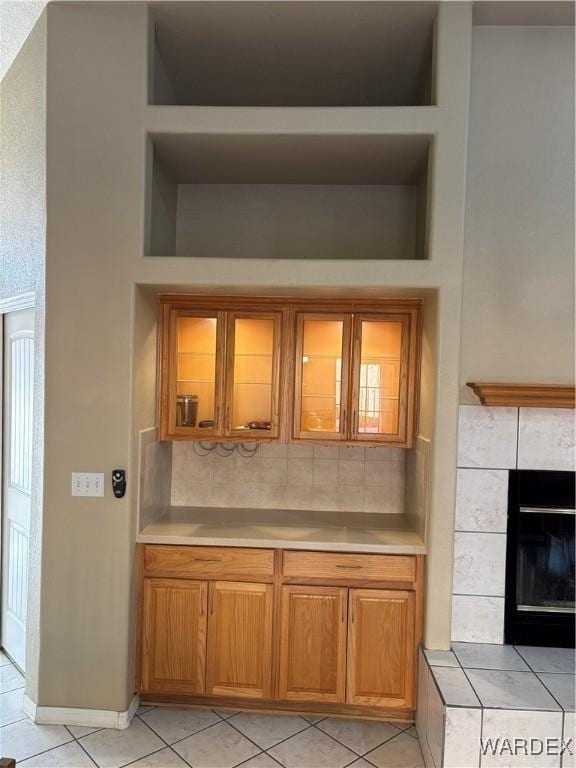 bar featuring light tile patterned floors, built in shelves, a tiled fireplace, and decorative backsplash