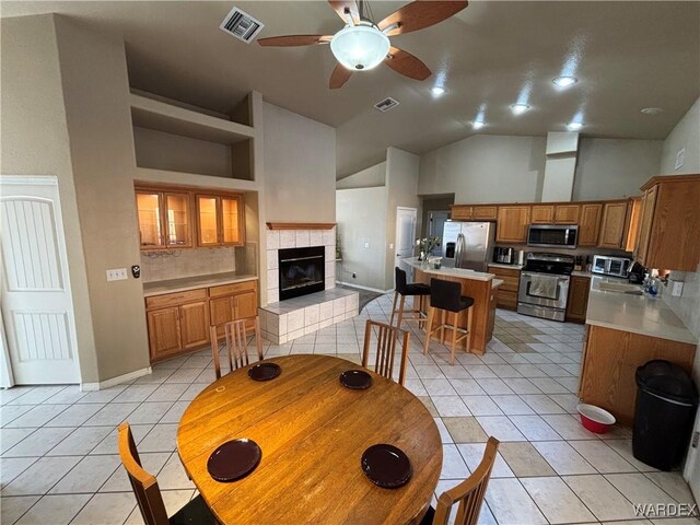 dining space featuring a tile fireplace, light tile patterned floors, high vaulted ceiling, a ceiling fan, and visible vents