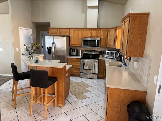 kitchen featuring appliances with stainless steel finishes, a towering ceiling, brown cabinetry, and a sink