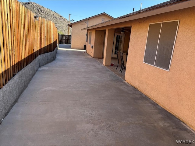 view of side of home with a patio, fence, stucco siding, and a ceiling fan