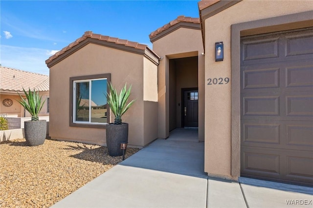 doorway to property featuring a garage, a tile roof, and stucco siding