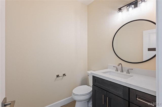 half bath featuring baseboards, vanity, and toilet