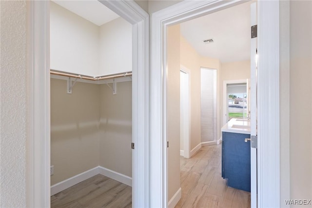 hall featuring light wood finished floors, baseboards, and visible vents