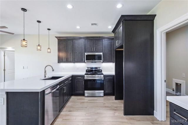 kitchen with stainless steel appliances, a peninsula, a sink, hanging light fixtures, and light countertops