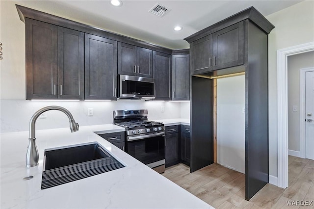 kitchen featuring light stone counters, light wood finished floors, visible vents, appliances with stainless steel finishes, and a sink