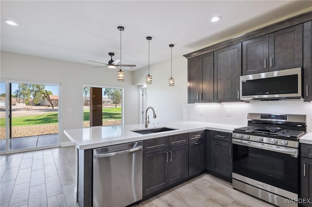 kitchen featuring appliances with stainless steel finishes, a peninsula, light countertops, pendant lighting, and a sink