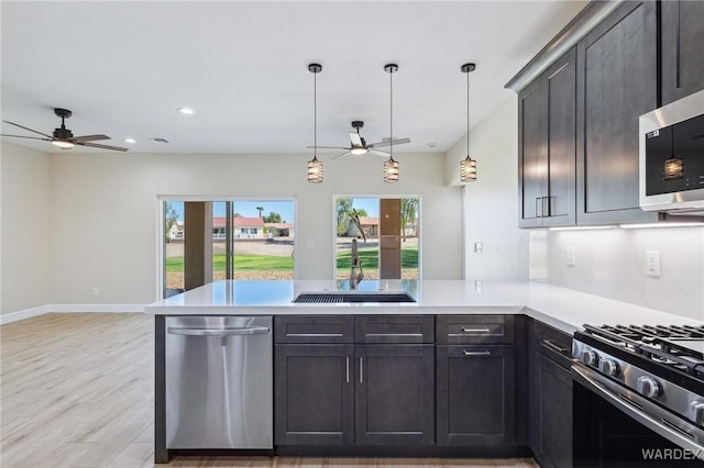 kitchen featuring decorative light fixtures, stainless steel appliances, light countertops, a sink, and a peninsula