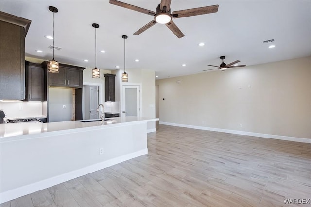 kitchen with dark brown cabinetry, a sink, visible vents, light countertops, and decorative light fixtures