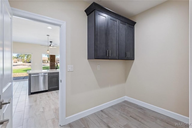 clothes washing area with ceiling fan, a sink, light wood-style flooring, and baseboards