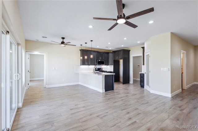 kitchen featuring light countertops, hanging light fixtures, light wood-style flooring, stainless steel microwave, and a peninsula