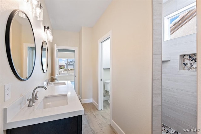 bathroom with double vanity, a sink, toilet, and baseboards