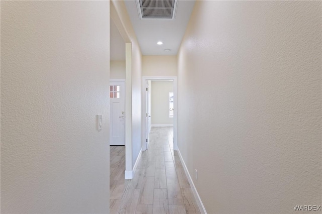 corridor with a textured wall, light wood-type flooring, visible vents, and baseboards