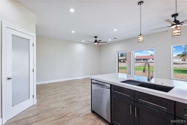 kitchen featuring decorative light fixtures, light countertops, light wood-type flooring, stainless steel dishwasher, and a sink