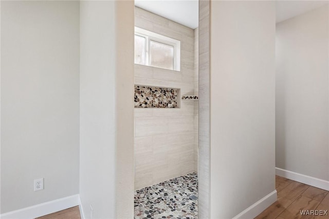 bathroom featuring baseboards, wood finished floors, and tiled shower