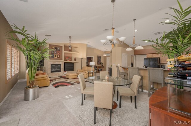 dining room featuring light colored carpet, visible vents, an inviting chandelier, vaulted ceiling, and a tile fireplace