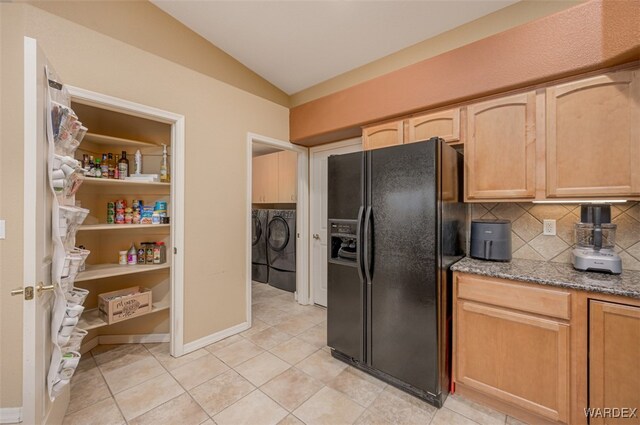 kitchen with lofted ceiling, stone counters, black fridge, light brown cabinetry, and washer and clothes dryer