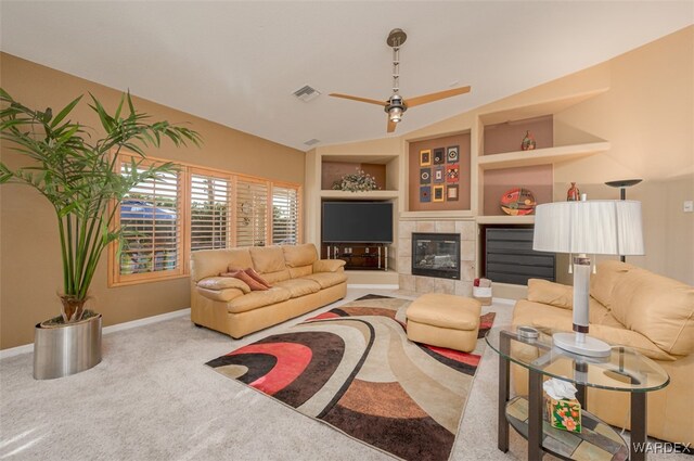 carpeted living area featuring ceiling fan, built in shelves, a tile fireplace, visible vents, and baseboards