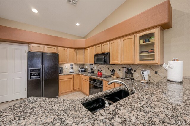 kitchen featuring stone counters, glass insert cabinets, light brown cabinets, a sink, and black appliances