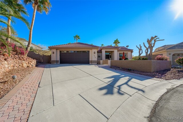 view of front of house with an attached garage, fence private yard, a tile roof, driveway, and stucco siding