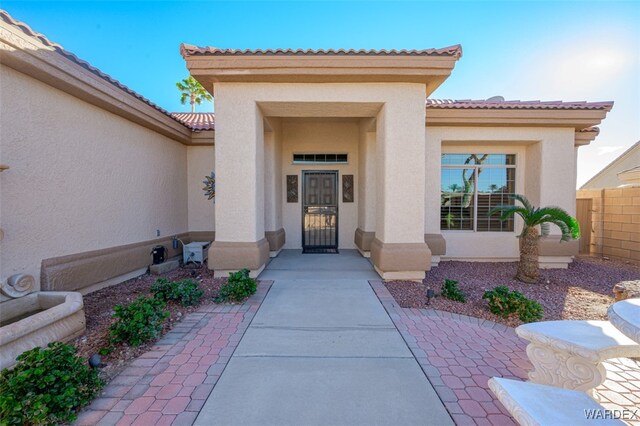 view of exterior entry featuring a tiled roof, fence, and stucco siding