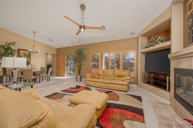 living area with a tile fireplace, ceiling fan with notable chandelier, light carpet, visible vents, and vaulted ceiling