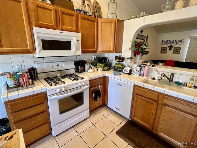 kitchen featuring white appliances, tile countertops, backsplash, a sink, and light tile patterned flooring