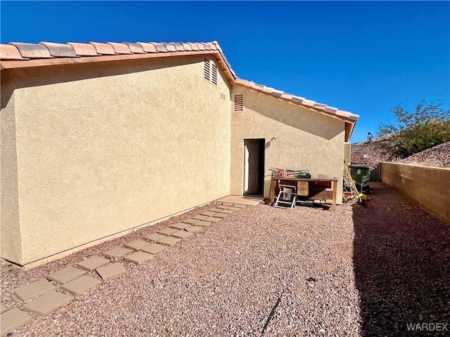 rear view of property with fence, a tile roof, and stucco siding