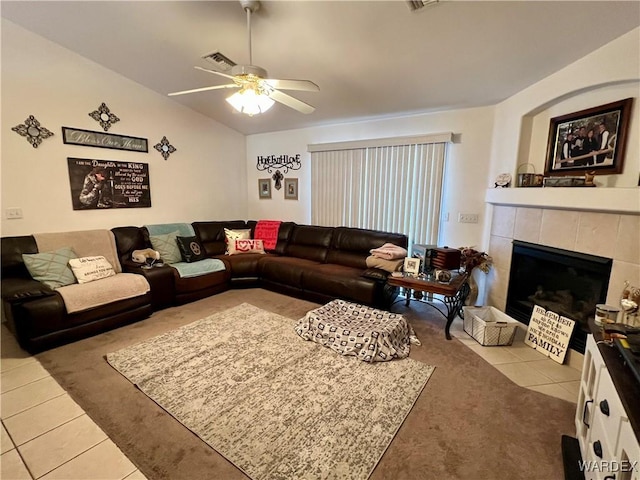 living area featuring light tile patterned floors, lofted ceiling, a tile fireplace, visible vents, and a ceiling fan