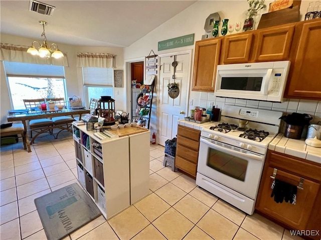 kitchen featuring white appliances, visible vents, tile countertops, lofted ceiling, and decorative light fixtures