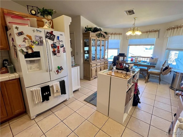 kitchen with visible vents, brown cabinetry, tile counters, white fridge with ice dispenser, and pendant lighting