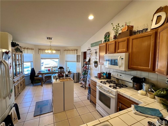 kitchen with white appliances, tasteful backsplash, visible vents, tile counters, and hanging light fixtures