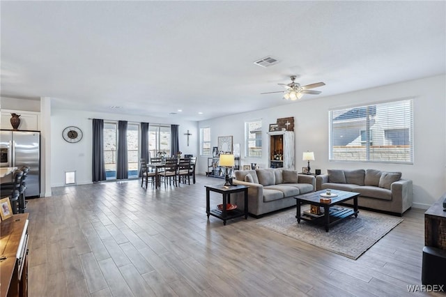 living area featuring light wood-style flooring, visible vents, ceiling fan, and baseboards