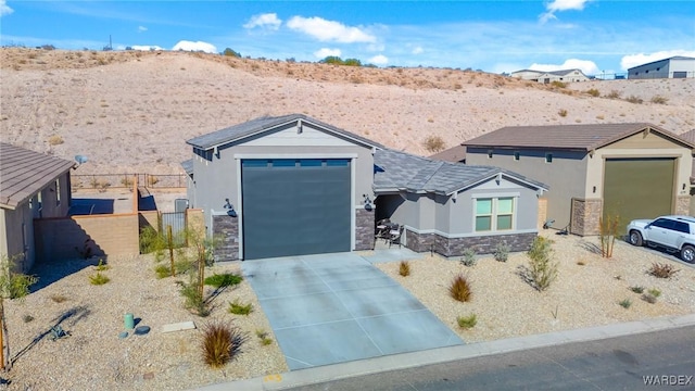 view of front of house with stucco siding, concrete driveway, an attached garage, fence, and stone siding