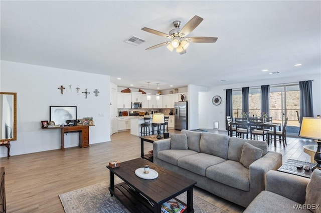 living room featuring light wood-style flooring, visible vents, a ceiling fan, and recessed lighting