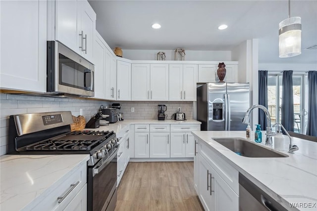 kitchen featuring stainless steel appliances, a sink, white cabinets, light stone countertops, and decorative light fixtures