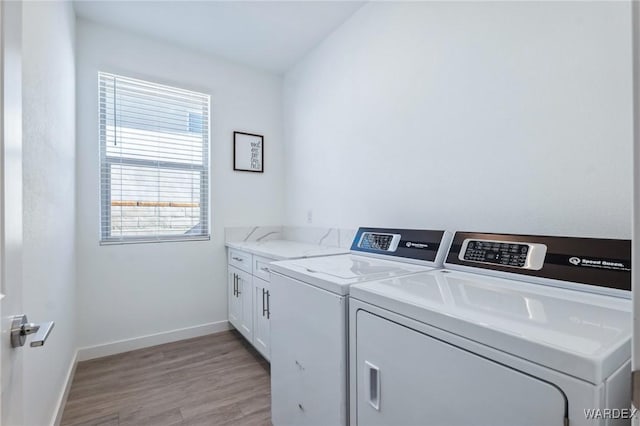 laundry room featuring light wood-style flooring, washer and clothes dryer, cabinet space, and baseboards