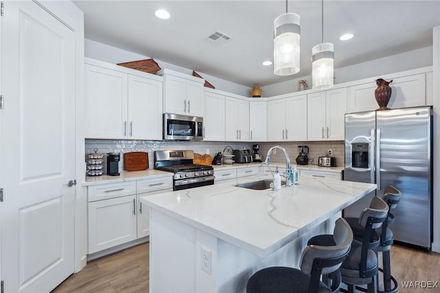 kitchen with light stone counters, decorative light fixtures, a sink, appliances with stainless steel finishes, and a center island with sink