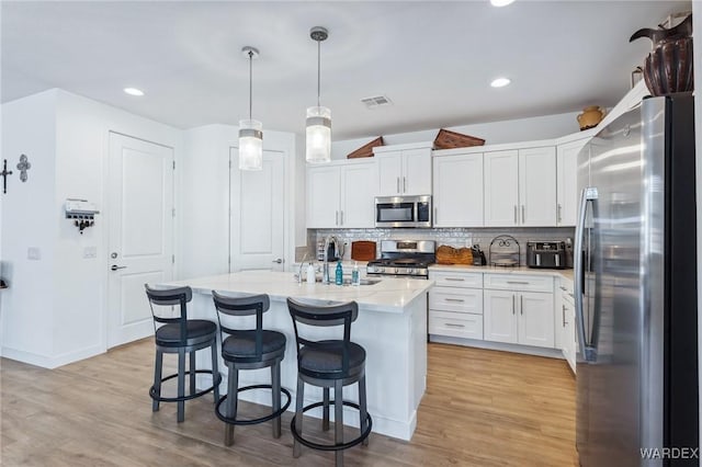 kitchen with decorative light fixtures, a center island with sink, stainless steel appliances, visible vents, and white cabinetry