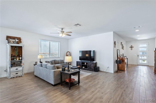 living area with light wood-type flooring, visible vents, and baseboards