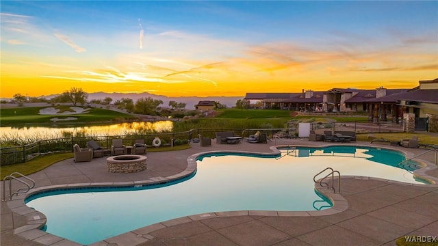 pool at dusk with an outdoor fire pit, a patio, a water view, a community pool, and fence