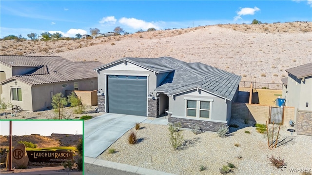 view of front of house with driveway, a garage, stone siding, fence, and stucco siding