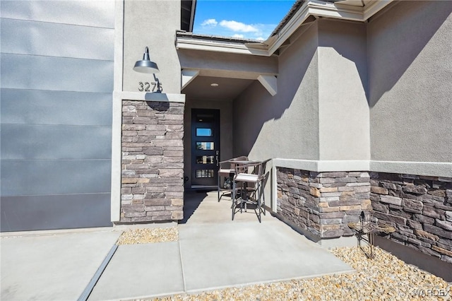 view of exterior entry with a garage, stone siding, a patio area, and stucco siding