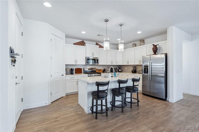 kitchen featuring a kitchen breakfast bar, white cabinets, appliances with stainless steel finishes, an island with sink, and pendant lighting