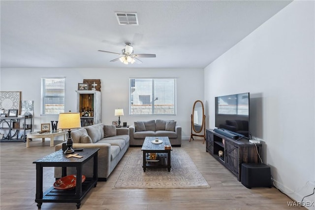 living room with light wood-type flooring, visible vents, ceiling fan, and baseboards