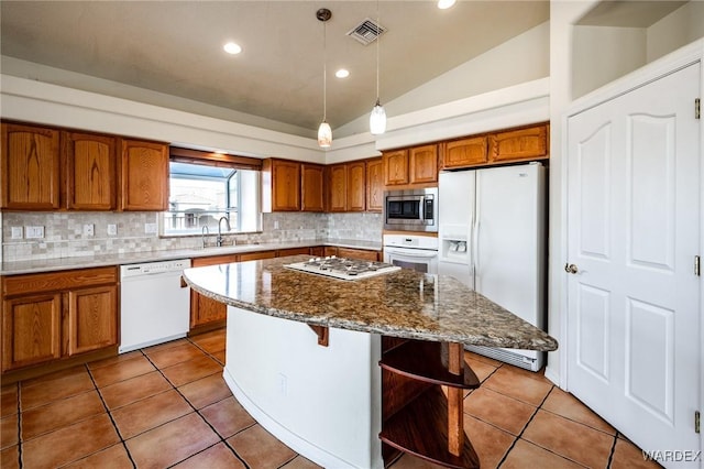 kitchen with white appliances, visible vents, brown cabinetry, a kitchen island, and a kitchen bar