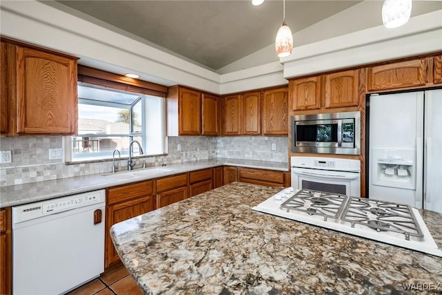 kitchen featuring brown cabinetry, white appliances, decorative light fixtures, and a sink