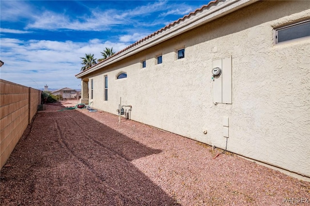 view of home's exterior featuring a tile roof, fence, and stucco siding