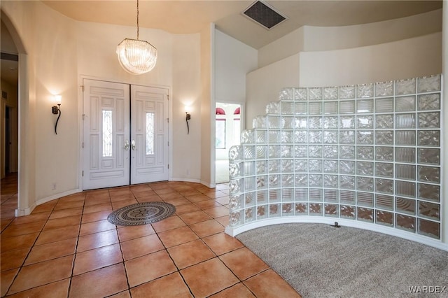 tiled entryway featuring arched walkways, a notable chandelier, visible vents, a high ceiling, and baseboards